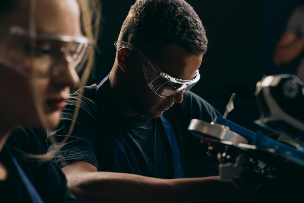 Students focused on robotics, wearing protective goggles, symbolizing teamwork and education in technology.